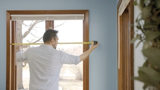 A man measuring the width of a window for replacement.