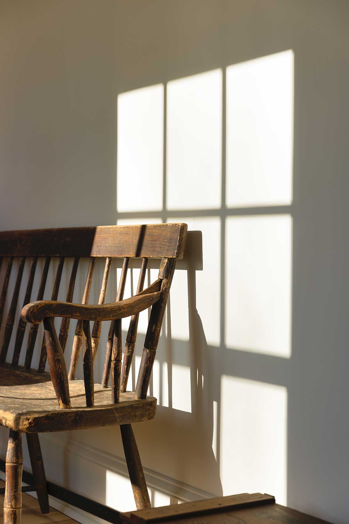 A wooden bench in a hallway with shadows from a window cast on the wall.