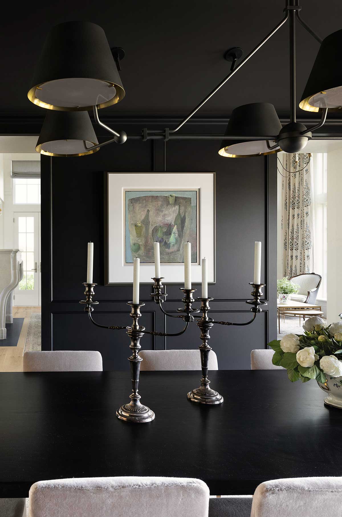 A formal dining room with black walls, black table, candles and white flowers.