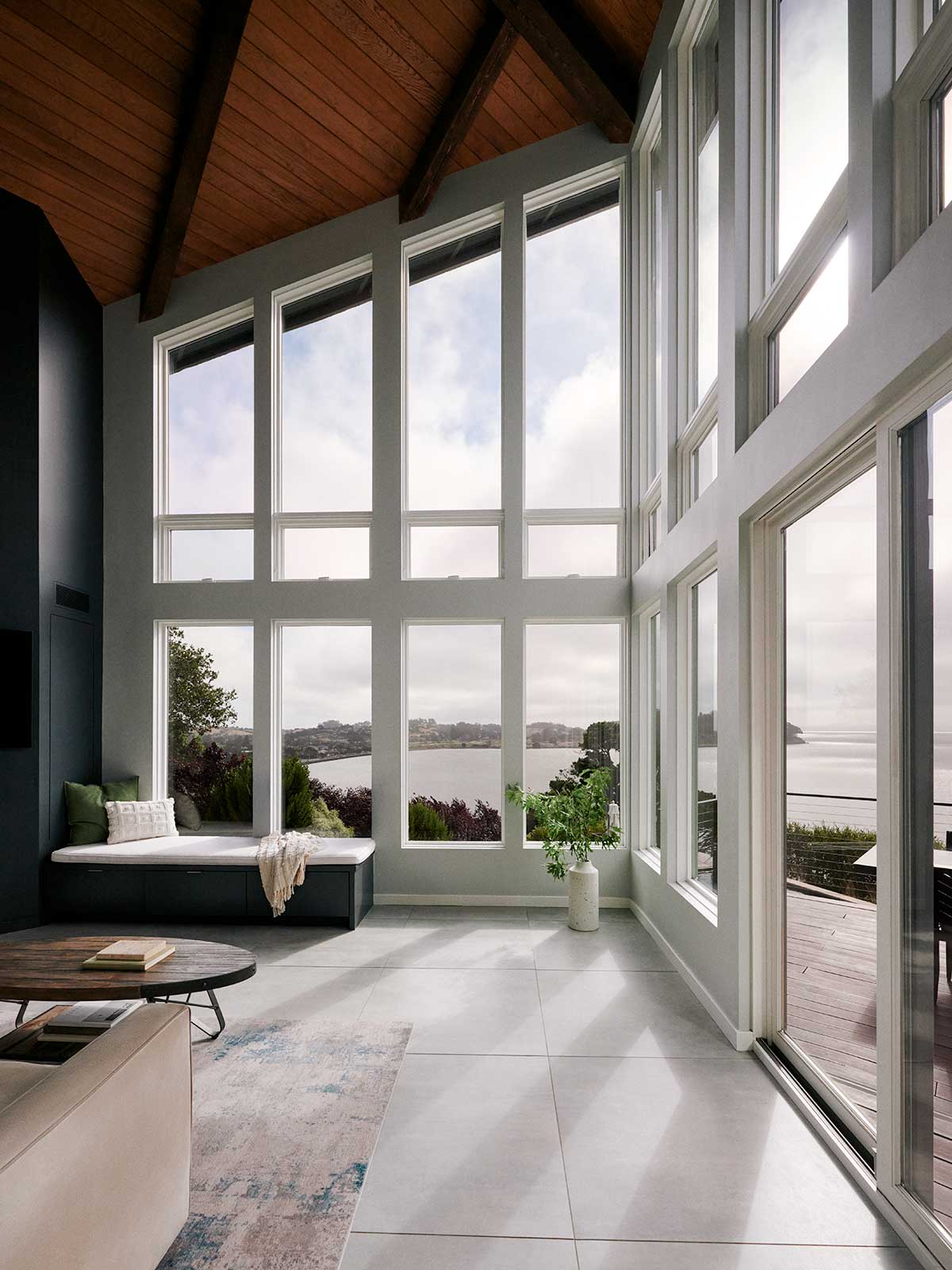 A living room featuring large a large wall of Marvin Ultimate Awning and Ultimate Polygon windows overlooking a bay in California.